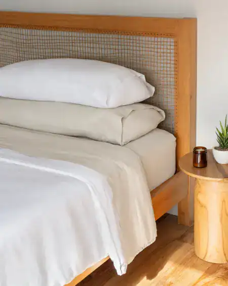 Grey and white bedding on a wooden bed frame with woven headboard in a cozy bedroom setting.