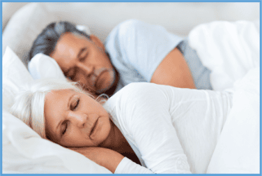 A man and woman peacefully sleeping on a bed with white bedding, demonstrating comfortable sleep and quality mattress support.